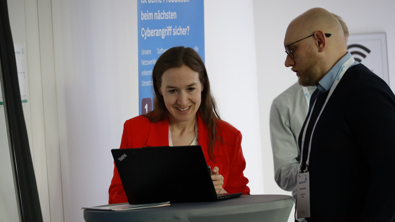 Eine Frau, mitwirkend in einem Start-up, steht mit einem Mann an einem Stehtisch. Sie unterhalten sich und schauen gemeinsam in ihren Laptop.